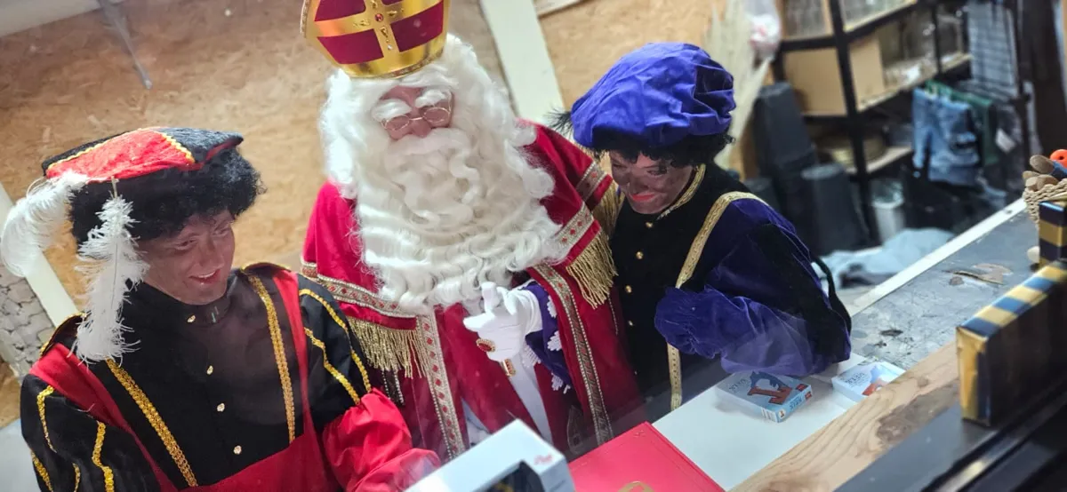 Sinterklaas en twee Pieten bekijken samen een cadeau